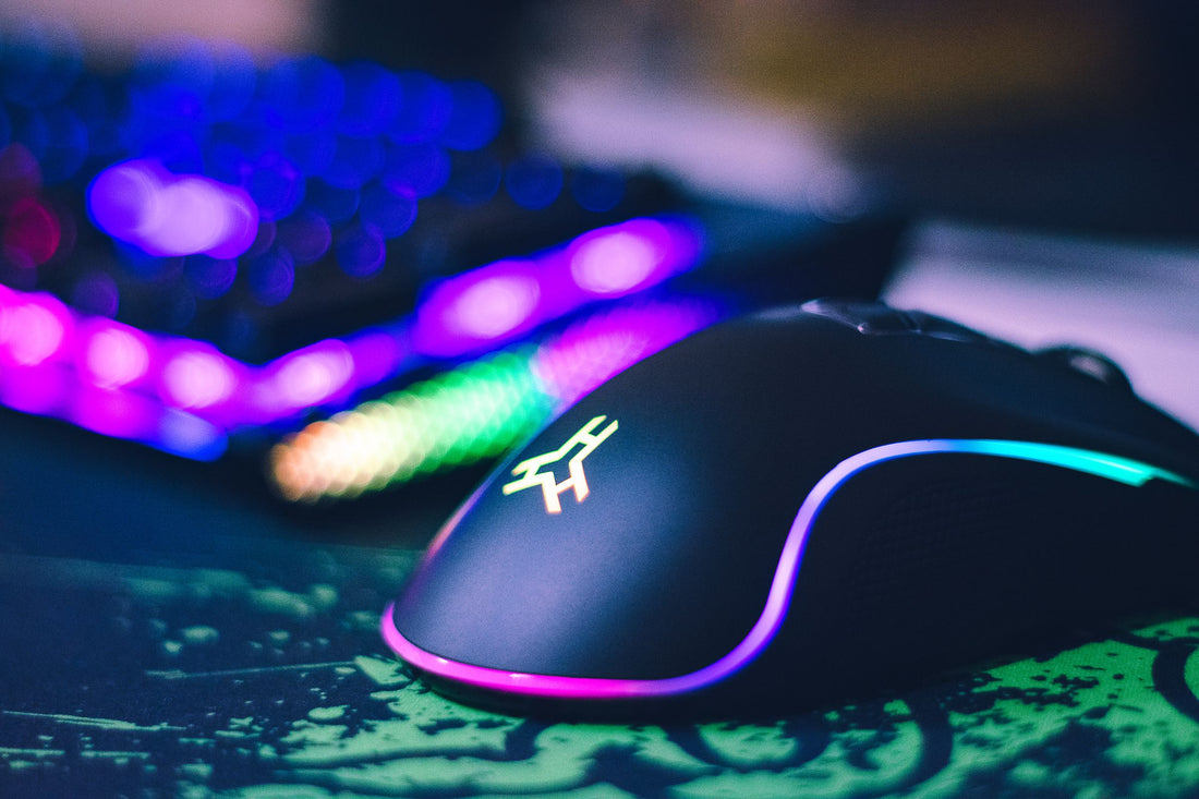 Close-up of a black RGB gaming mouse glowing on a desk with a mechanical keyboard blurred in the background