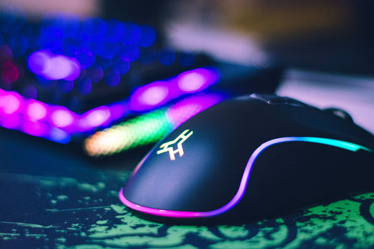 Close-up of a black RGB gaming mouse glowing on a desk with a mechanical keyboard blurred in the background