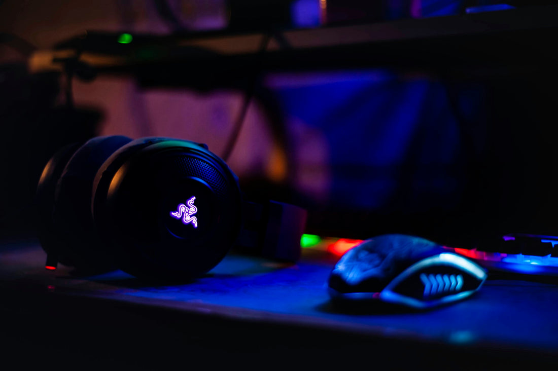 Black Razer gaming headset with glowing RGB logo next to a gaming mouse on a dark desk