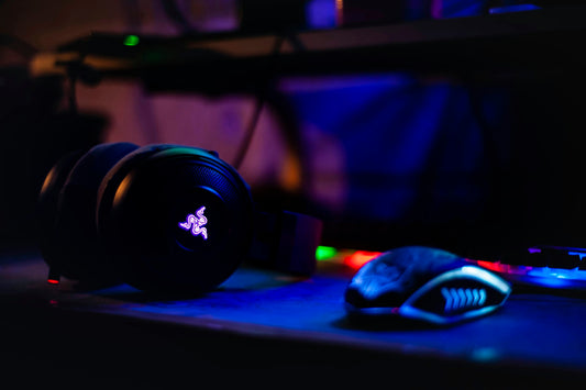 Black Razer gaming headset with glowing RGB logo next to a gaming mouse on a dark desk
