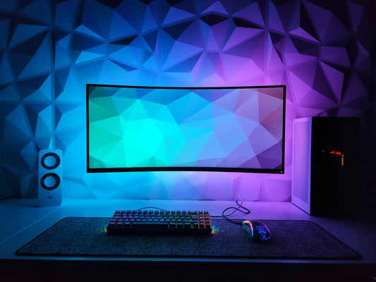 Curved ultrawide gaming monitor glowing with RGB colors on a desk with mechanical keyboard and mouse