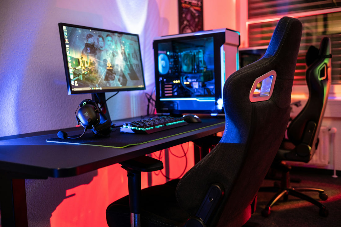 Black racing-style gaming chair with cutout headrest next to an RGB-lit gaming desk setup
