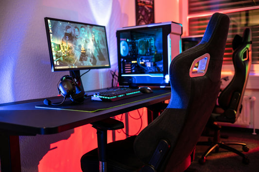 Black racing-style gaming chair with cutout headrest next to an RGB-lit gaming desk setup